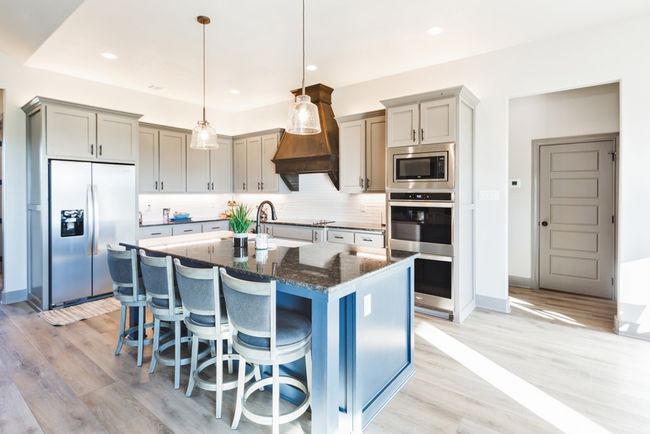 Kitchen with appliances with stainless steel finishes, a kitchen island with sink, dark stone countertops, light wood-type flooring, and backsplash | Image 4