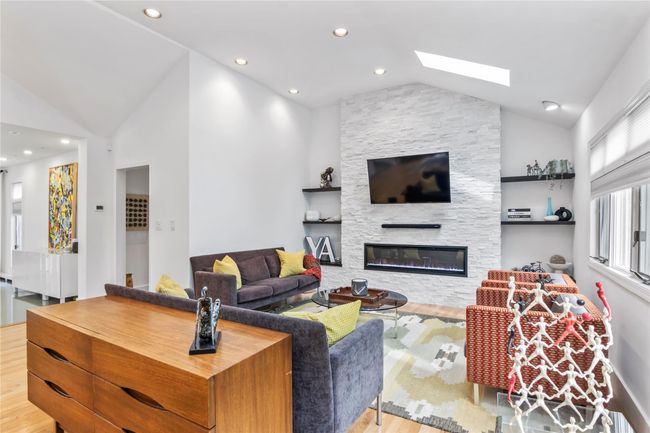 Living area with wood finished floors, a skylight, a fireplace, recessed lighting, and high vaulted ceiling | Image 11