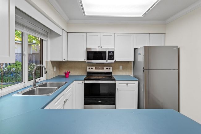 Kitchen featuring white cabinetry, tasteful backsplash, crown molding, a sink, and appliances with stainless steel finishes | Image 5