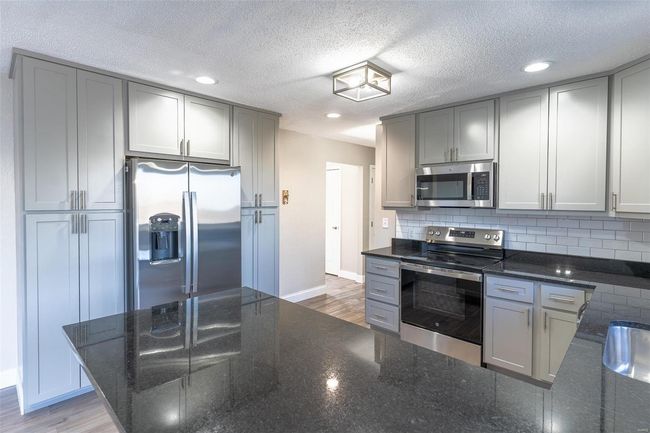Kitchen with appliances with stainless steel finishes, a textured ceiling, light / wood-style floors, and gray cabinets | Image 40