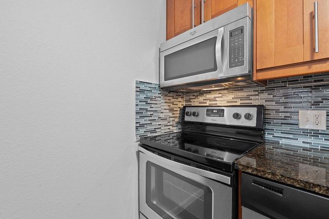 Kitchen featuring dark stone countertops, tasteful backsplash, appliances with stainless steel finishes, and brown​​‌​​​​‌​​‌‌​‌‌​​​‌‌​​‌‌​‌​​​​​‌ cabinetry | Image 4