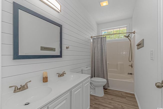 Full bathroom featuring toilet, double vanity, wood finished floors, shower / bath combo with shower curtain, and wooden walls | Image 17