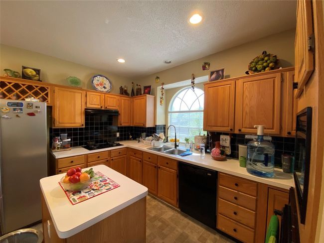 Kitchen with stainless steel fridge, backsplash, stovetop, black dishwasher, and a kitchen island | Image 21