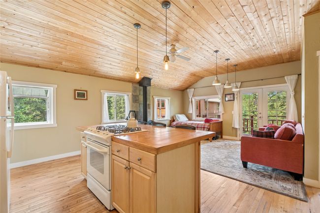 Apartment kitchen with white appliances, wood counters, light brown cabinets, wooden ceiling, and a wood stove | Image 49