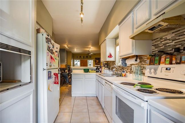 Kitchen featuring white appliances, a sink, light countertops, under cabinet range hood, and tasteful backsplash | Image 10