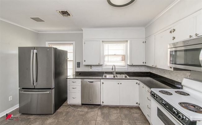 Kitchen featuring a sink, dark countertops, visible vents, white cabinets, and appliances with stainless steel finishes | Image 13