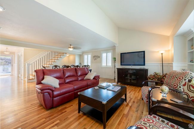 Living room with vaulted ceiling, stairway, crown molding, wainscoting, and wood finished floors | Image 15