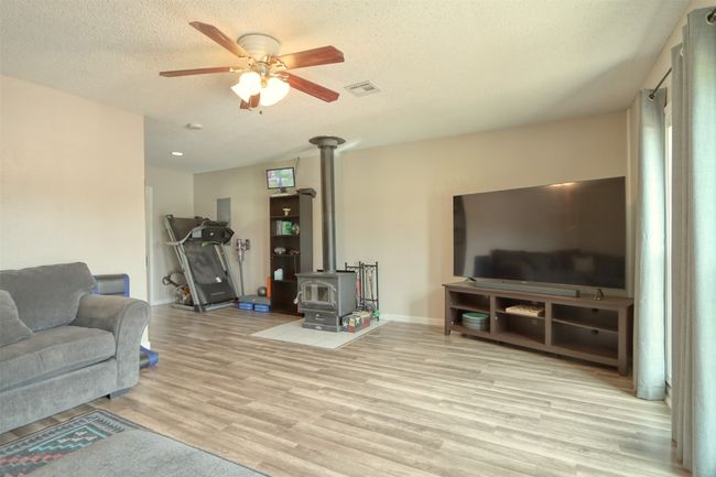 Living area with a wood stove, ceiling fan, wood finished floors, and a textured ceiling | Image 25