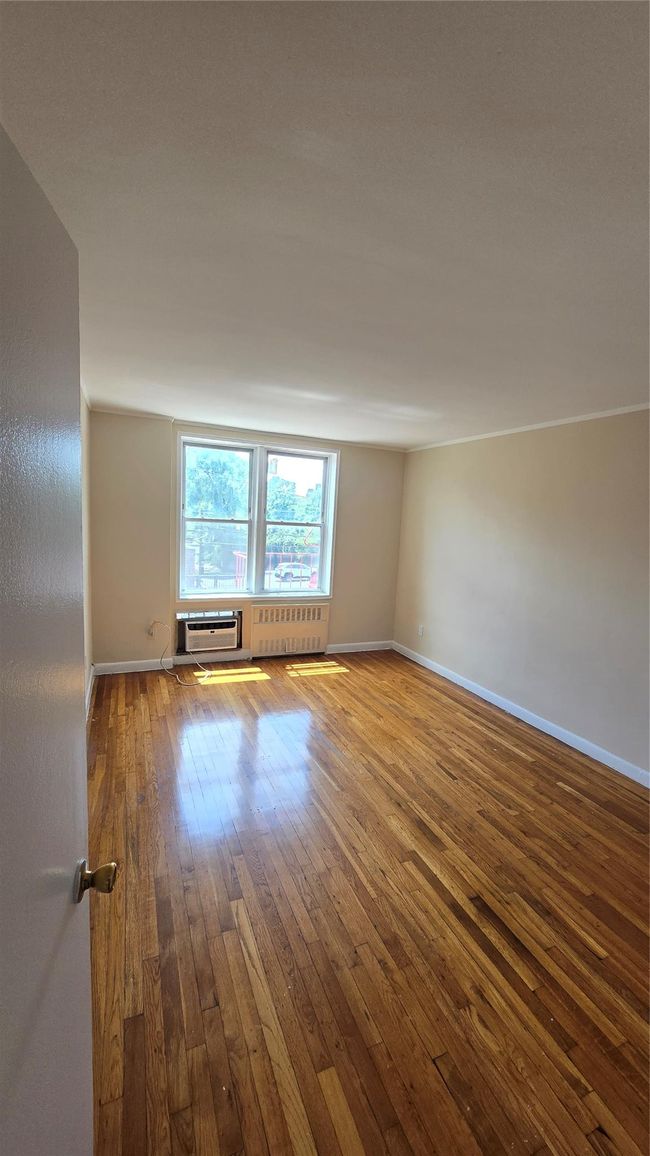 Empty room with wood-type flooring, an AC wall unit, and radiator heating unit | Image 7