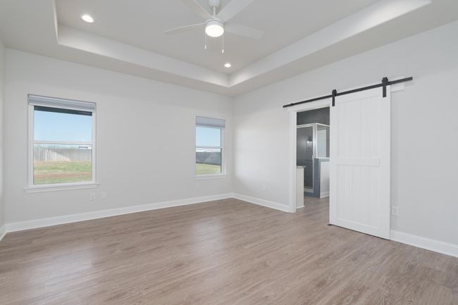 primaryy with baseboards, a barn door, ceiling fan, light wood-style floors, and a tray ceiling | Image 19