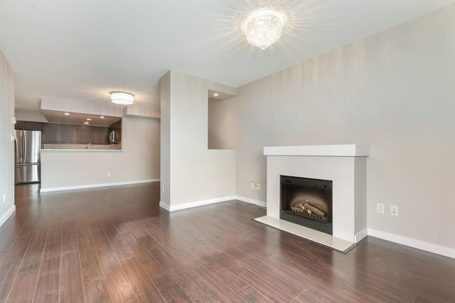 Unfurnished living room featuring dark wood-style floors, a fireplace with raised hearth, and a chandelier | Image 7