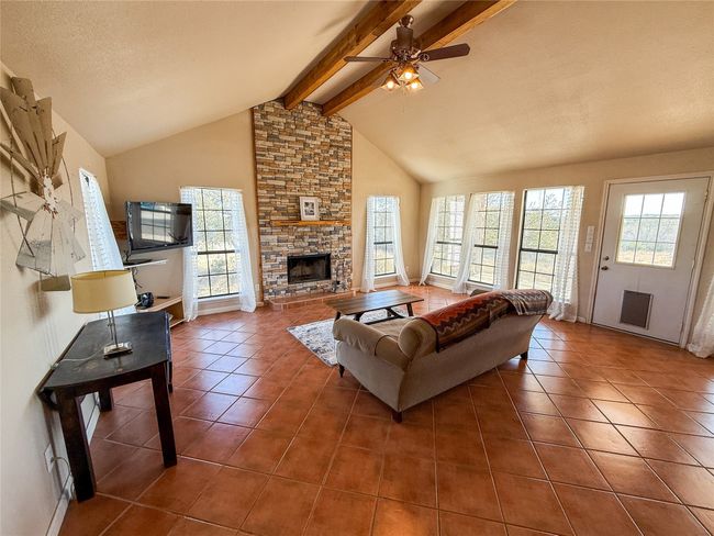 Living room featuring high vaulted ceiling, beam ceiling, a ceiling fan, a stone fireplace, and tile patterned flooring | Image 9