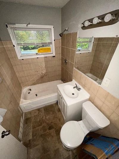 Full bathroom featuring toilet, vanity, tiled shower / bath combo, and tile walls | Image 2