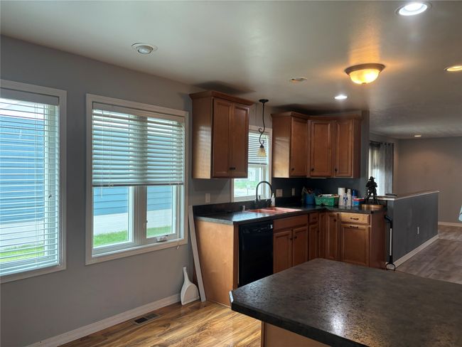 Kitchen with a sink, dark countertops, black dishwasher, light wood-type flooring, and baseboards | Image 13