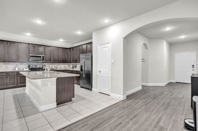 Kitchen featuring stainless steel appliances, dark brown cabinetry, tasteful backsplash, arched walkways, and light stone countertops | Image 9