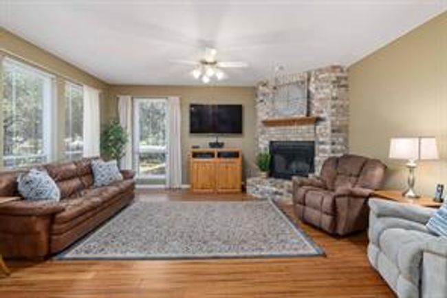 Living area with a ceiling fan, wood finished floors, and a fireplace | Image 9