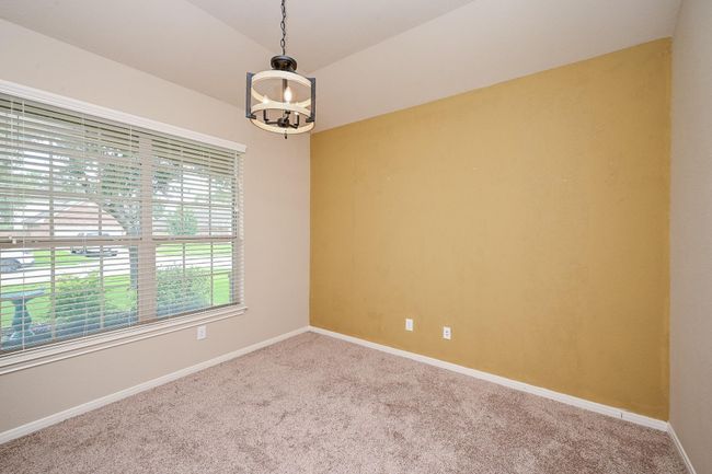 This home office features a large window with blinds providing natural light, a cozy carpeted floor, and a stylish hanging light fixture. A warm accent wall complements the neutral tones, creating a welcoming space. | Image 5