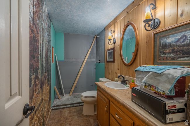 Bathroom with a textured ceiling, vanity, a shower, and wooden walls | Image 51