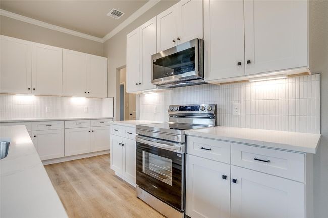 Kitchen featuring white cabinets, appliances with stainless steel finishes, ornamental molding, and visible vents | Image 14