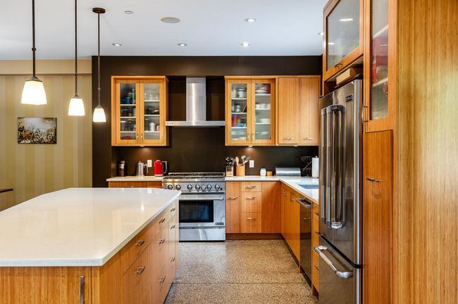 Kitchen with wall chimney range hood, stainless steel appliances, light countertops, dark aggregate flooring, and a center island | Image 12