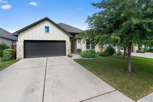 View of front of home featuring board and batten siding, a front yard, driveway, an attached garage, and brick siding | Image 35