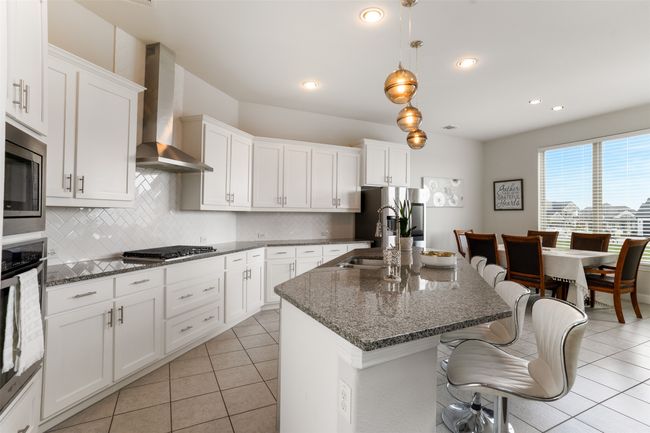 Kitchen with stainless steel appliances, wall chimney range hood, light tile patterned floors, a kitchen bar, and tasteful backsplash | Image 11