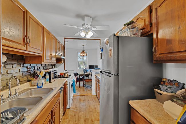 Kitchen featuring freestanding refrigerator, light countertops, ceiling fan, light wood-style flooring, and brown cabinetry | Image 4