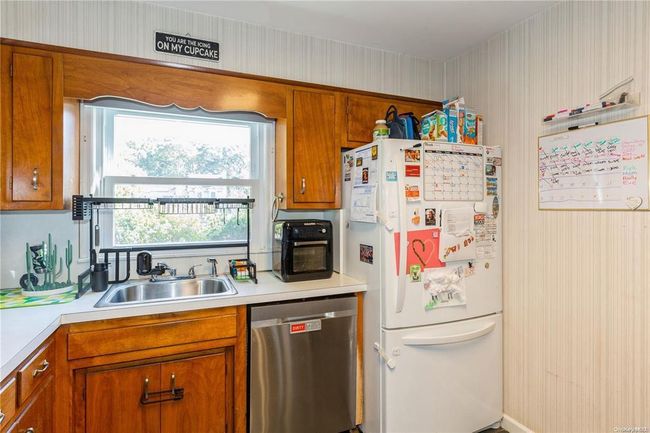 Kitchen with stainless steel dishwasher, a sink, brown cabinets, light countertops, and freestanding refrigerator | Image 17
