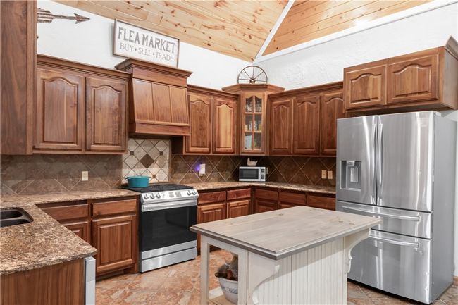 Kitchen featuring vaulted ceiling, decorative backsplash, appliances with stainless steel finishes, a kitchen island, and light stone counters | Image 5