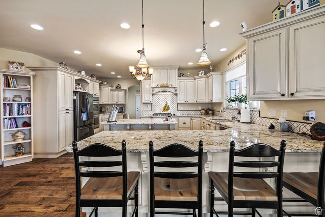 Kitchen with a breakfast bar, dark wood-type flooring, sink, decorative light fixtures, and stainless steel fridge with ice dispenser | Image 34