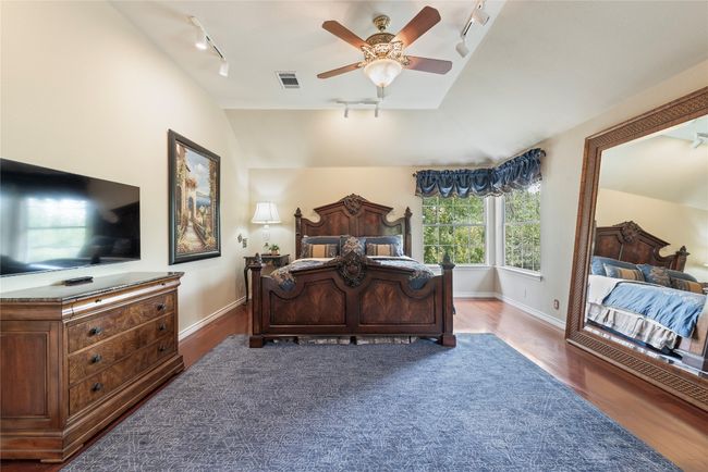 Spacious primary bedroom with vaulted ceiling, wood flooring, and elegant traditional finishes. | Image 26