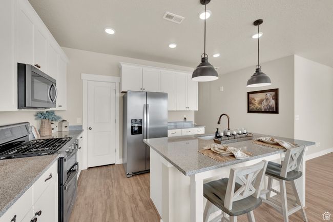 Kitchen with appliances with stainless steel finishes, light wood-type flooring, a sink, a kitchen island with sink, and white cabinets | Image 10