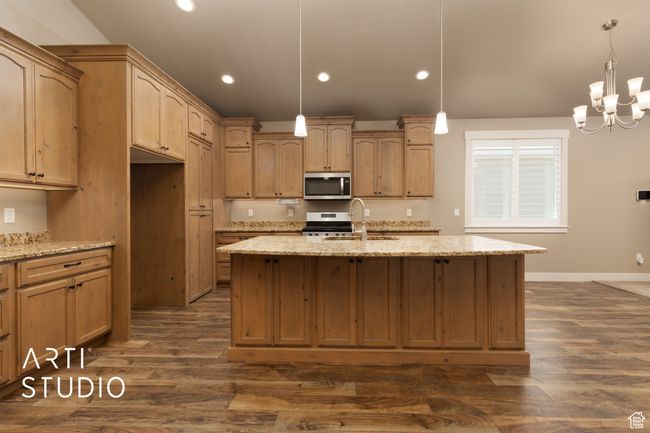 Kitchen featuring stainless steel appliances, recessed lighting, dark wood-type flooring, light stone countertops, and a center island with sink | Image 14