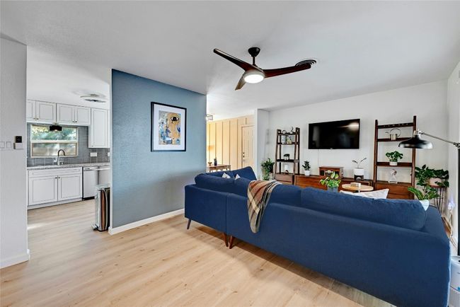 The cozy living room is complete with a modern ceiling fan with easy access to the kitchen/dining areas. | Image 8