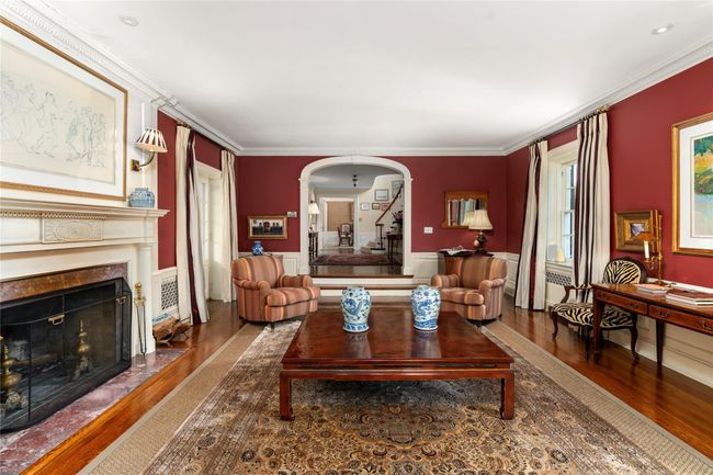 Living area with wood finished floors, arched walkways, crown molding, a fireplace, and stairs | Image 5