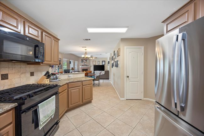 Kitchen with black appliances, a chandelier, light tile patterned floors, a peninsula, and decorative backsplash | Image 14