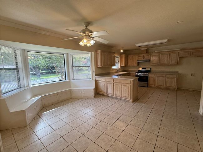 Kitchen featuring light tile patterned floors, stainless steel gas range oven, crown molding, a peninsula, and a textured ceiling | Image 5