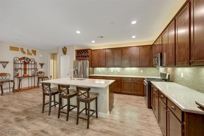 Kitchen with backsplash, a kitchen breakfast bar, stainless steel appliances, a kitchen island with sink, and light wood-style floors | Image 12