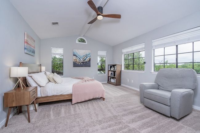 Bedroom with vaulted ceiling with beams, baseboards, visible vents, light colored carpet, and a ceiling fan. | Image 17