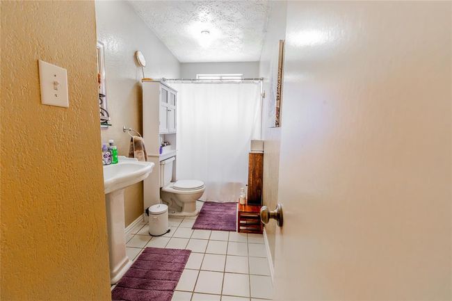 This secondary bathroom features a simple design with a pedestal sink, tub, and a toilet. It has light walls, a tiled floor, providing a cozy and clean atmosphere. | Image 20
