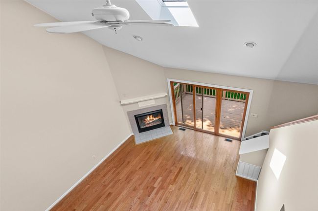 Unfurnished living room featuring a tile fireplace, wood finished floors, a ceiling fan, vaulted ceiling, and a skylight | Image 20