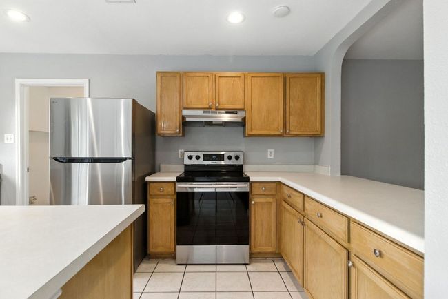 Kitchen with stainless steel appliances, under cabinet range hood, light countertops, light tile patterned floors, and recessed lighting | Image 8