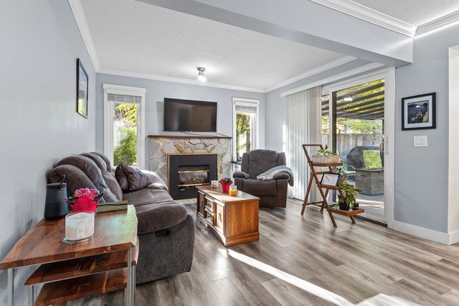 Living area featuring wood finished floors, a healthy amount of sunlight, a stone fireplace, and ornamental molding | Image 11