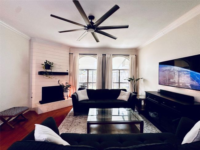 Living room with a large fireplace, ornamental molding, a ceiling fan, and wood finished floors | Image 5