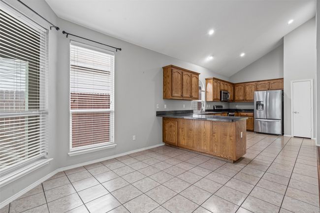 Kitchen featuring stainless steel appliances, a peninsula, light tile patterned floors, brown cabinets, and lofted ceiling | Image 27