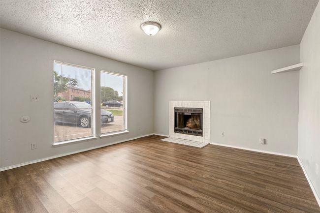 Unfurnished living room with wood finished floors, a textured ceiling, a tile fireplace, and baseboards | Image 4