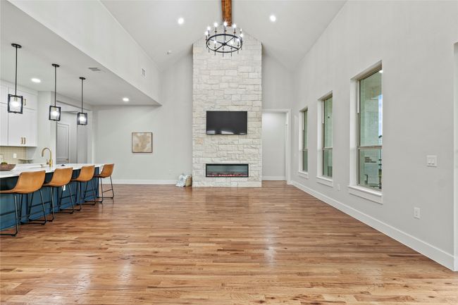 Living room with high vaulted ceiling, light wood-style flooring, a fireplace, a chandelier, and wet bar | Image 6