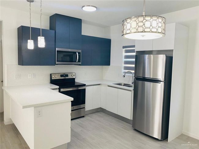Kitchen featuring stainless steel appliances, a peninsula, backsplash, light countertops, and pendant lighting | Image 6