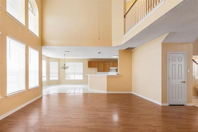 Unfurnished living room with a high ceiling, light wood-type flooring, baseboards, stairs, and a notable chandelier | Image 7