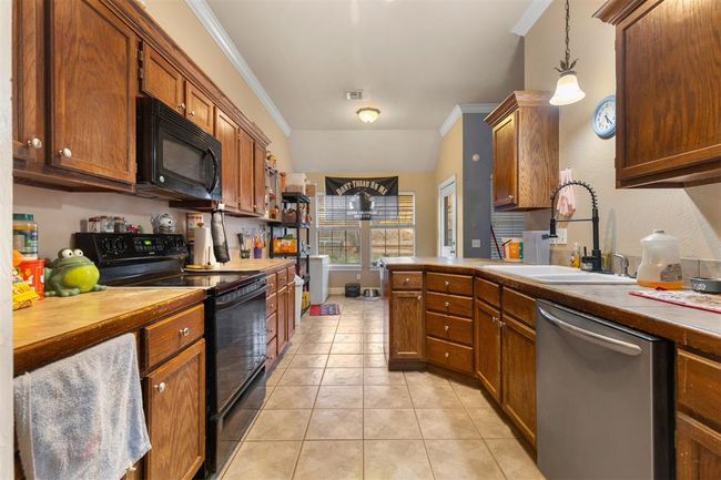 Kitchen with sink, crown molding, black appliances, light tile patterned flooring, and decorative light fixtures | Image 7